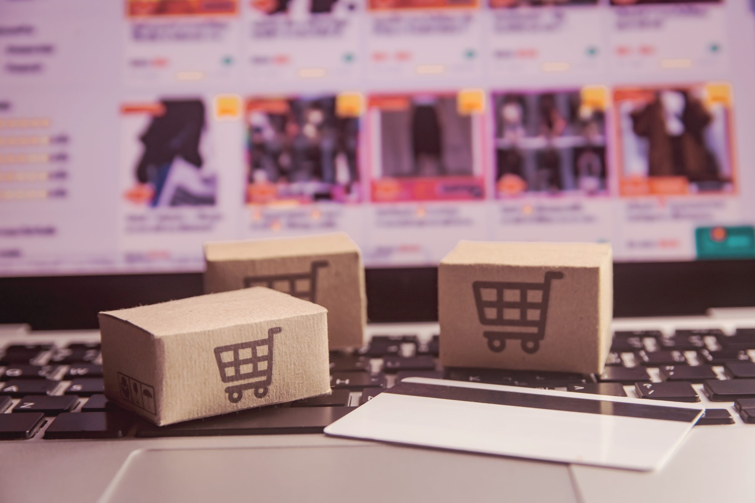 Small cardboard boxes with shopping cart icons on a laptop keyboard, symbolizing e-commerce shipping.
